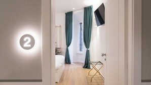 Ein Hotelzimmer mit Bett, einem an der Wand montierten Fernseher und einem Fenster mit Vorhängen.