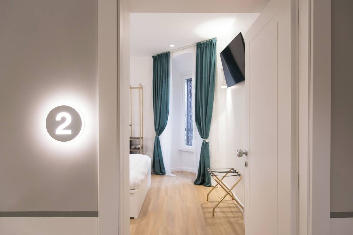 A hotel room with a bed, a wall-mounted TV, and a window with curtains.