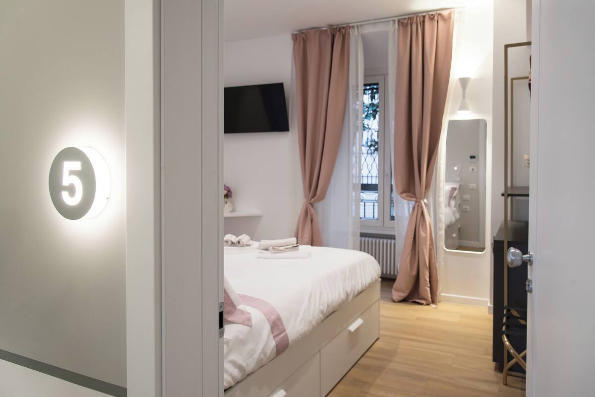 A modern bedroom with a bed, a TV mounted on the wall, and a number '5' sign.