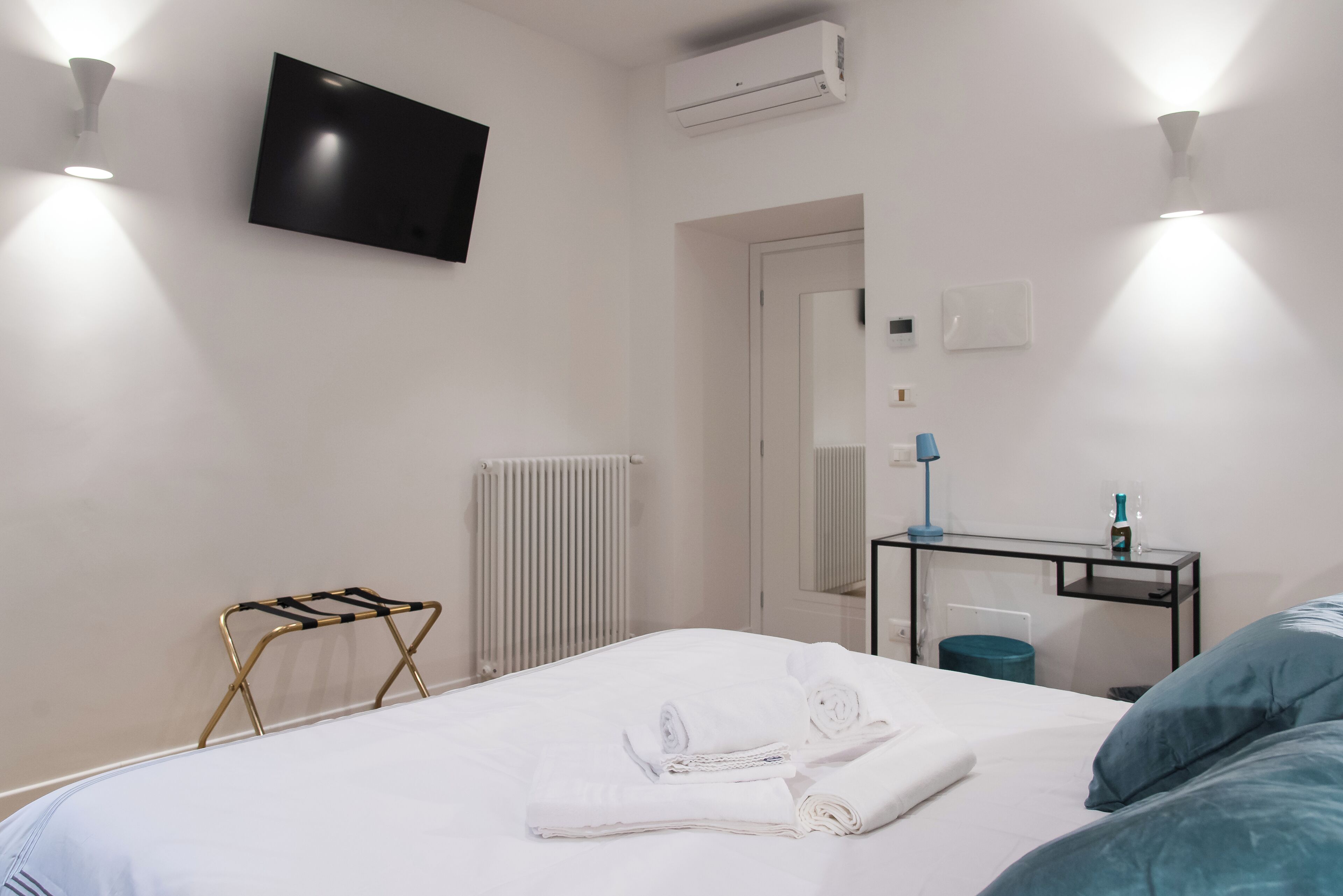 A hotel room with a bed, a TV mounted on the wall, a desk with a chair, and a radiator.