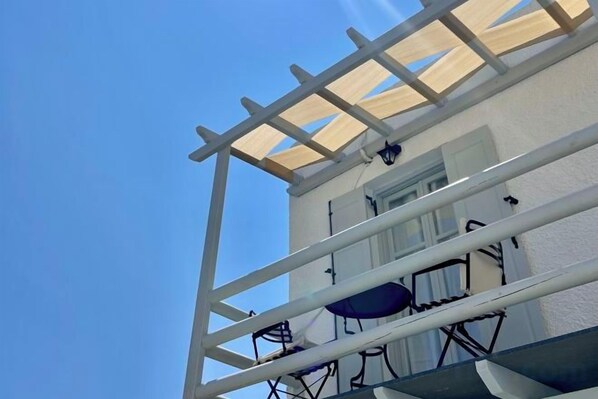 Un bâtiment à l’extérieur blanc, doté d’un balcon avec une balustrade blanche, et un ciel bleu clair en arrière-plan.