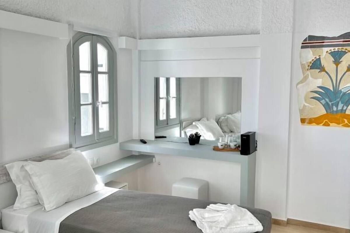 A modern bedroom with a bed, a bedside table, a mirror, and a window.