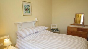 Une chambre à coucher avec un lit, une table de chevet, une commode, une chaise et un tableau au mur.