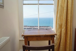A room with a view of the sea through a window, a wooden table, and a chair.