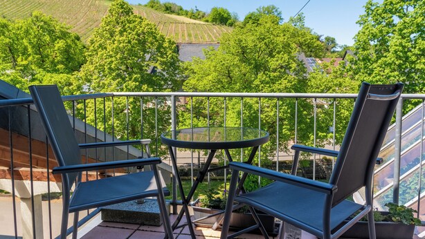 A balcony with two chairs and a small table, overlooking a vineyard and trees.