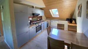 A modern kitchen with a skylight, wooden ceiling, and a dining area with a table and chairs.