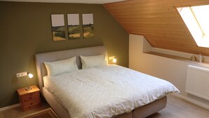 A bedroom with a bed, a nightstand, a wall-mounted lamp, and a window with a view of the countryside.