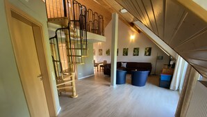 A spacious living area with a wooden staircase, a sofa, and two blue trash bins.