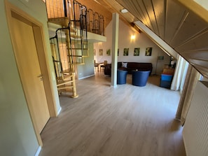 En rummelig opholdsstue med en trætrap, en sofa og to blå skraldespande.