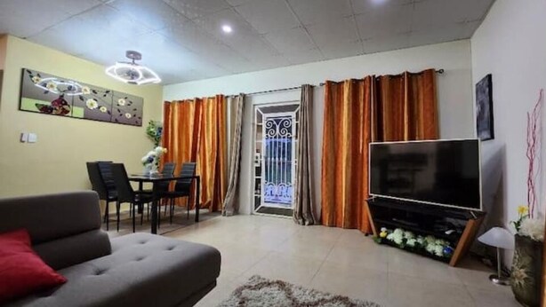 A living room with a sofa, TV, and dining area. - Breezy Bungalow Airport Suite (Piarco)