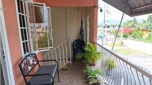 A covered balcony with a stone floor, a metal railing, a bench, and potted plants. - Breezy Bungalow Airport Suite (Piarco)