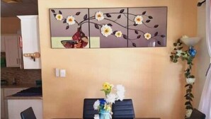 A dining area with a table, chairs, a decorative wall piece, and a ceiling fan. - Breezy Bungalow Airport Suite (Piarco)