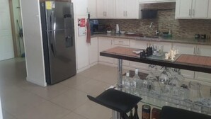 A kitchen with white cabinets, a stainless steel refrigerator, a microwave, and a tiled backsplash. - Breezy Bungalow Airport Suite (Piarco)
