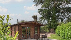 Een houten chalet met een terras, voorzien van een tafel en stoelen, omgeven door groen.