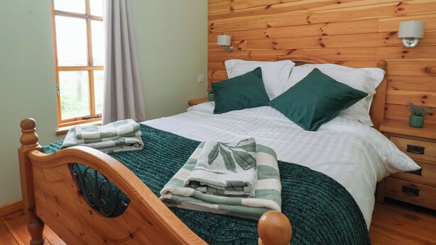 Een slaapkamer met houten lambrisering, een bed, kussens en een nachtkastje.