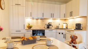 Une cuisine moderne avec des meubles blancs, une table à manger dressée avec des assiettes, des tasses et un panier de pain.