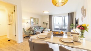 Un salon moderne comprenant un coin repas, un ensemble de canapés, une table basse et une grande fenêtre avec des rideaux.