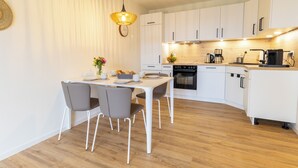 Une cuisine moderne avec des meubles blancs, un plan de travail en bois et un coin repas comprenant une table et des chaises blanches.