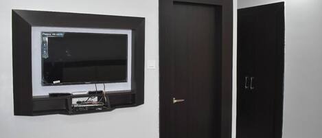 Una habitación con un televisor montado en la pared, una puerta cerrada y una cama con una colcha roja.