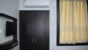 Ein Zimmer mit einer schwarzen Tür, einem Wand-Fernseher, einer Klimaanlage und einem Fenster mit gelbem Vorhang.