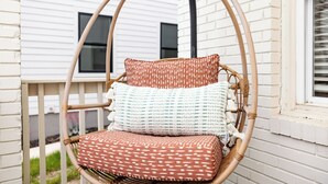 A wicker swing chair with patterned cushions against a white brick wall. - Optimist Abode 2: Chic Stay in the Queen City, walking distance to Optimist Hall (Charlotte)