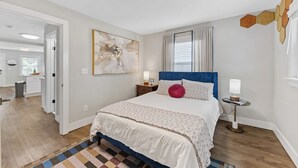 A bedroom with a large bed, a bedside table with a lamp, a wall-mounted artwork, and a view of the adjacent bathroom. - Optimist Abode 2: Chic Stay in the Queen City, walking distance to Optimist Hall (Charlotte)