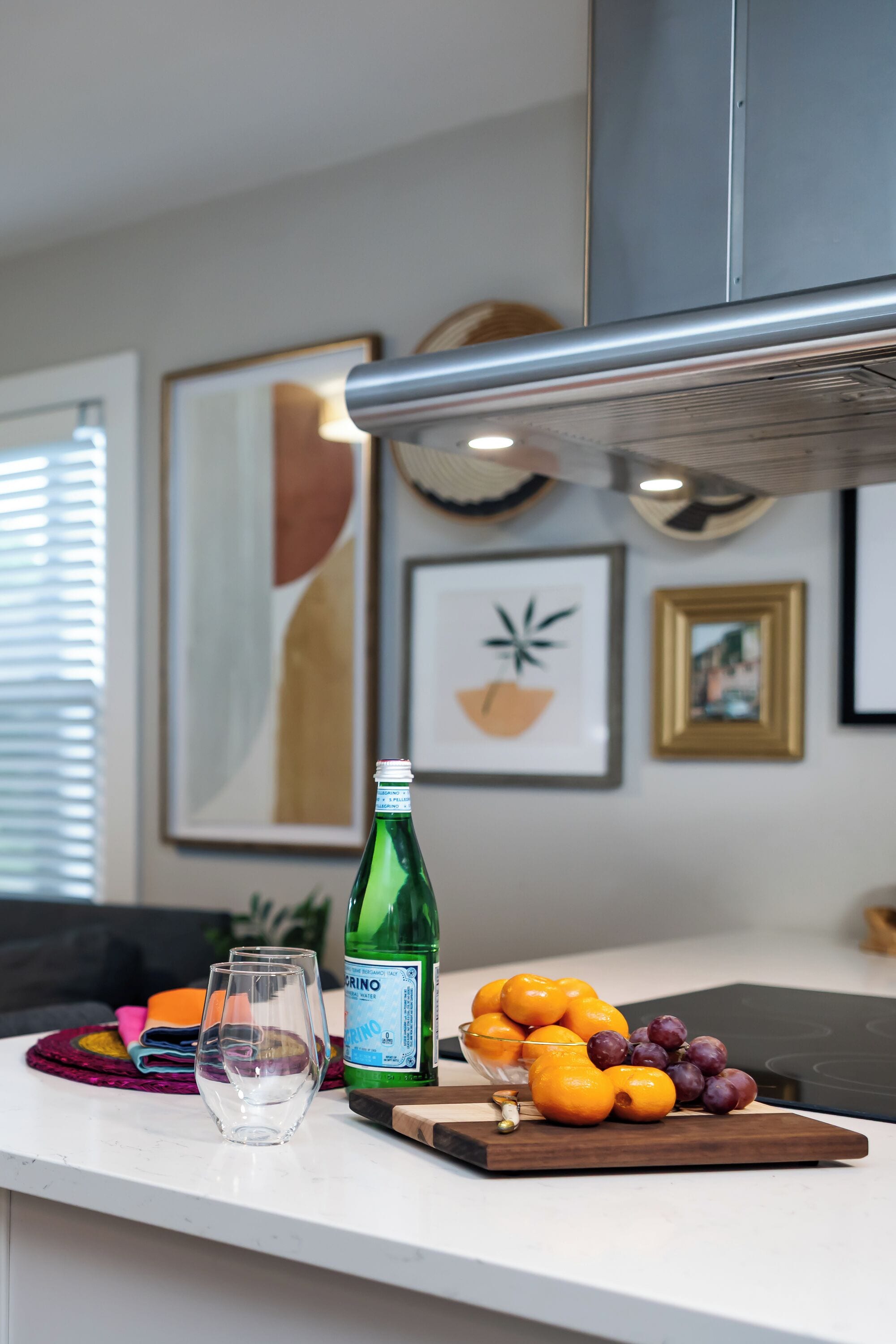A kitchen counter with a bottle of green liquor, a glass, oranges, and grapes.