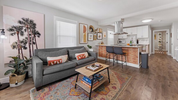 A modern living room with a grey sofa, a coffee table, and a kitchen area with white cabinets and a bar. - Optimist Abode 2: Chic Stay in the Queen City, walking distance to Optimist Hall (Charlotte)