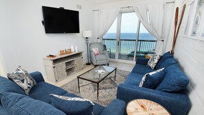 Un salon comprenant un ensemble de canapés, une table basse, un téléviseur et une vue sur la mer depuis un balcon.