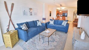 Un salon avec deux canapés bleus, une table basse en verre, un meuble en bois et un ventilateur de plafond.
