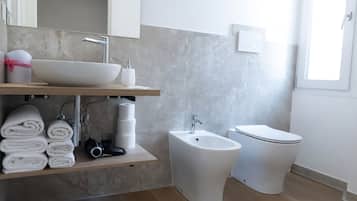 A modern bathroom with a sink, bidet, toilet, and a towel rack.