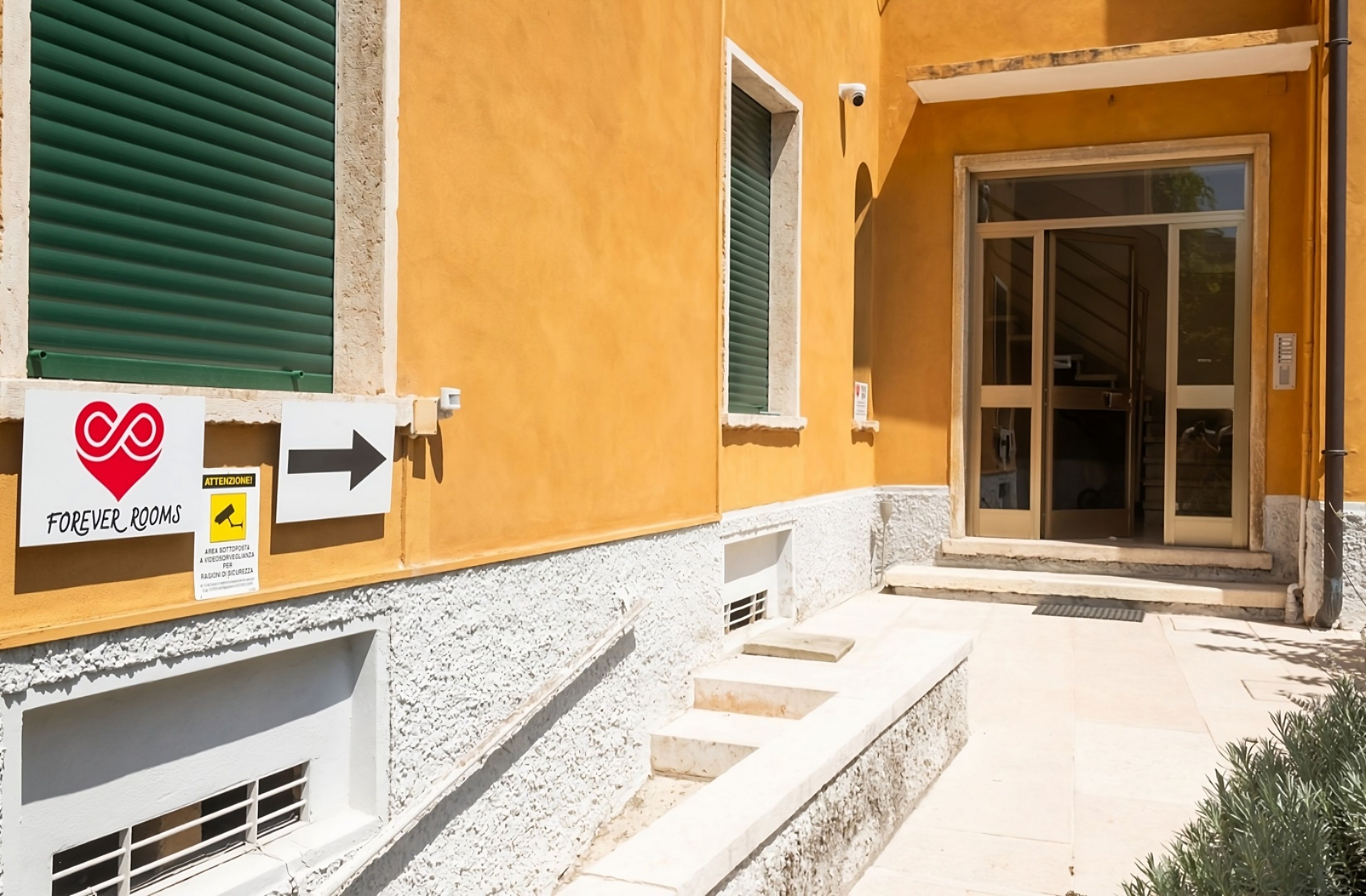A building with a yellow exterior, a sign indicating 'FOREVER ROOMS', and a staircase leading to a door with glass panels.
