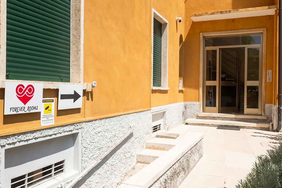 A building with a yellow exterior, a sign indicating 'FOREVER ROOMS', and a staircase leading to a door with glass panels.