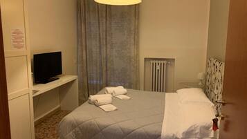 A hotel room with a bed, a television on a stand, a radiator, and a door.