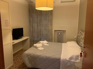 Une chambre d’hôtel avec un lit, un téléviseur posé sur un meuble, un radiateur et une porte.