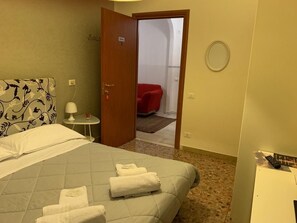 A hotel room with a bed, a bedside table with a lamp, a red chair in the adjacent room, and a round mirror on the wall. - Il Giardino di Gioia (Verona)
