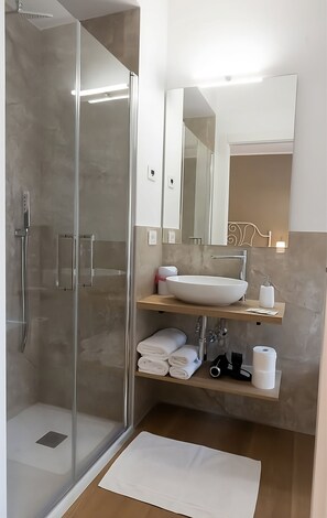 A modern bathroom with a glass-enclosed shower, a large white sink, and a mirror above the sink.