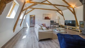 An attic living room with exposed wooden beams, a sofa, a TV, and a fireplace. - Gite with swimming pool le Bervic (Sainte-Croix)