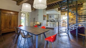 A spacious dining area with a wooden table and chairs, a staircase, and a kitchen in the background. - Gite with swimming pool le Bervic (Sainte-Croix)