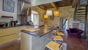 A kitchen with a central island, stone walls, a staircase, and a purple sofa. - Gite with swimming pool le Bervic (Sainte-Croix)