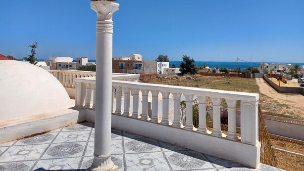 Un balcon doté d’une balustrade blanche, donnant sur un quartier résidentiel et la mer.