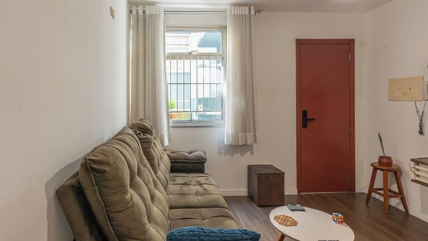 A living room with a sofa, a small table with a puzzle, a red door, and a window with curtains. - Apto c boa Localiza o Prox Centro pet Friendly (Jundiai)
