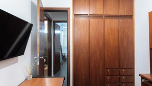 A room with a wooden wardrobe, a flat-screen TV mounted on the wall, and a small table with a vase. - Apto c boa Localiza o Prox Centro pet Friendly (Jundiai)