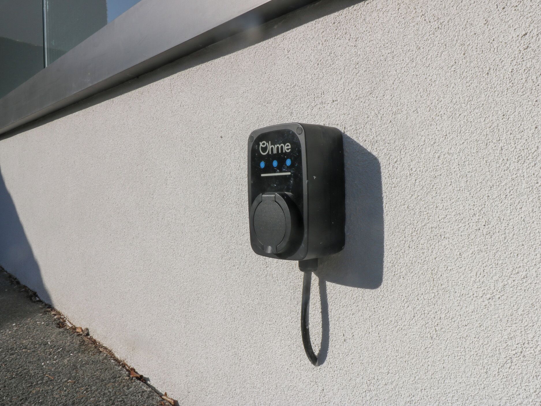 Eine schwarze Ladestation für den Außenbereich mit dem Aufdruck "Ohme", montiert an einer strukturierten Wand.