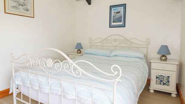 Une chambre avec un lit en métal blanc, deux tables de chevet avec des lampes, une fenêtre donnant sur le ciel et deux tableaux encadrés accrochés au mur.