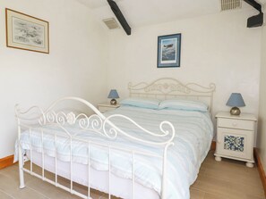 Ein Schlafzimmer mit weißem Metallbettgestell, zwei Nachttischen inklusive Lampen, einem Fenster mit Blick zum Himmel und zwei gerahmten Bildern an der Wand.