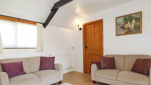 Un salon spacieux avec deux canapés beige, un tapis blanc, une porte en bois et un tableau accroché au mur.