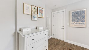 A hallway with a white dresser, framed artwork on the wall, and a door.