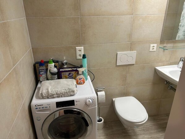 A compact bathroom with a washing machine, toilet, and sink.