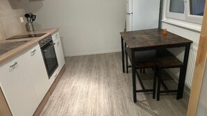 A compact kitchen with white cabinets, a built-in oven, and a wooden table with a bench.